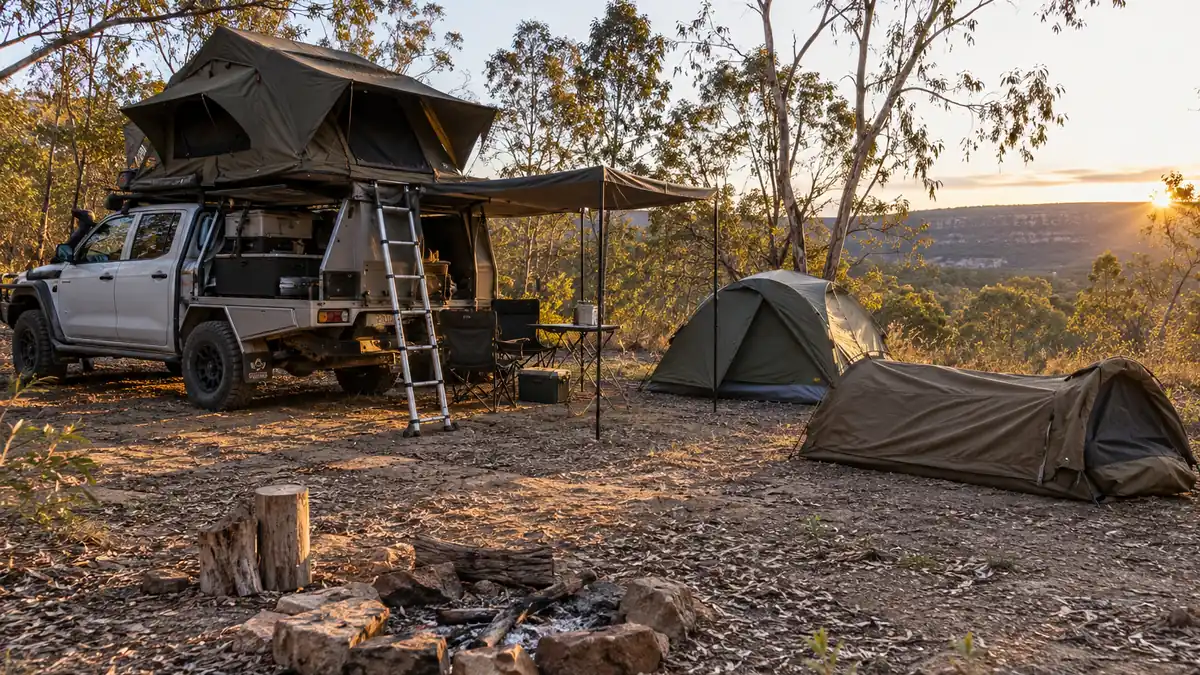 4WD ute with an open rooftop tent beside a dome tent and a canvas swag at a dry bush campsite