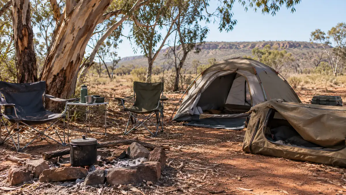 Tent and canvas swag set up beside camp chairs and a fire ring under gum trees